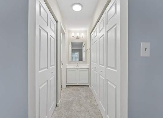A long hallway with white doors and a light switch on the wall.