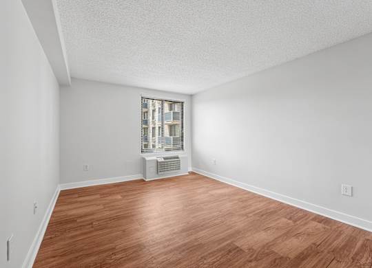 A room with wooden flooring and a window with a view of a cityscape.