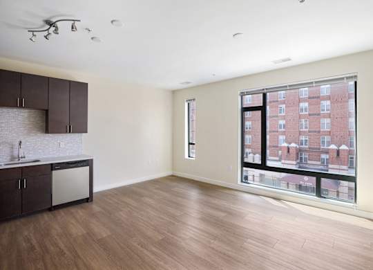 A large empty room with a kitchen area and a window overlooking a building at The Maxwell Apartments, Arlington