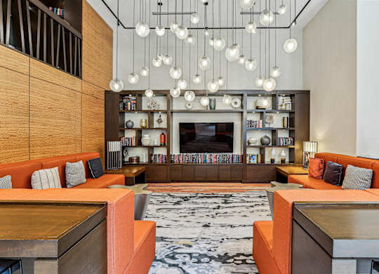 A modern living room with orange couches and a large television at The Maxwell Apartments, Arlington
