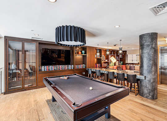 A pool table is in the middle of a room with a bar and a bookshelf in the background at The Maxwell Apartments, Arlington