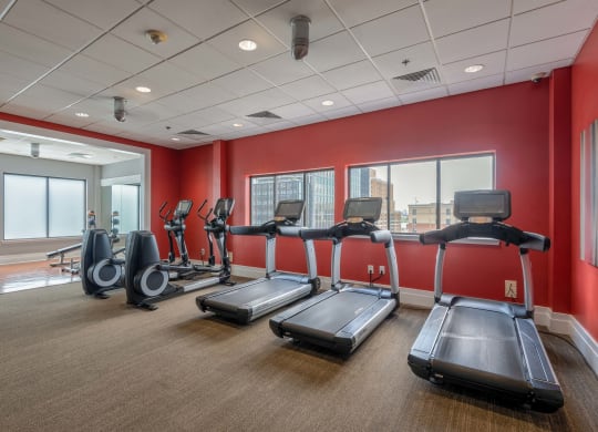 a gym with cardio equipment and red walls and windows