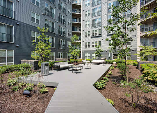 A modern outdoor seating area with benches and trees is surrounded by apartment buildings.