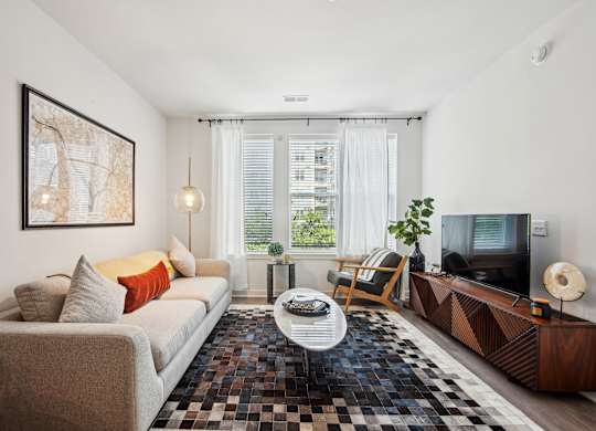 A living room with a beige couch, a black and white checkered rug, a wooden cabinet, and a flat screen TV.
