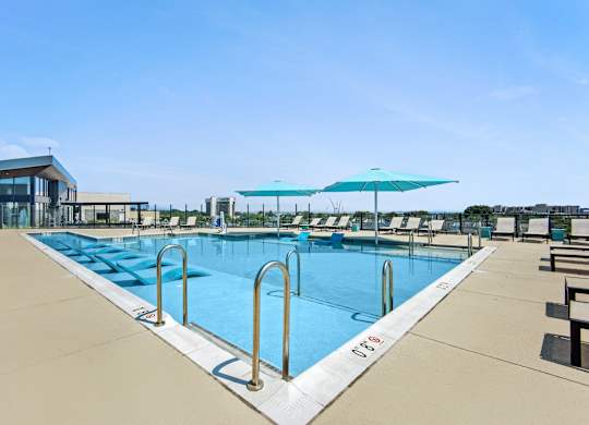 A large outdoor swimming pool with sun loungers and umbrellas.