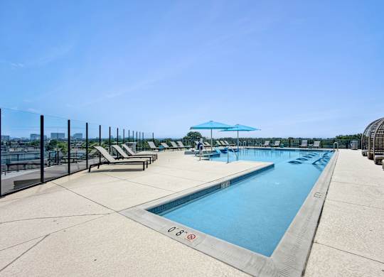 A large outdoor swimming pool with sun loungers and a clear blue sky.