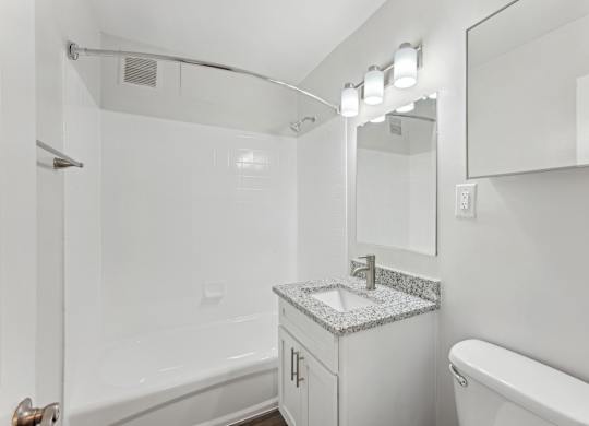 A white bathroom with a marble counter top and a white toilet.