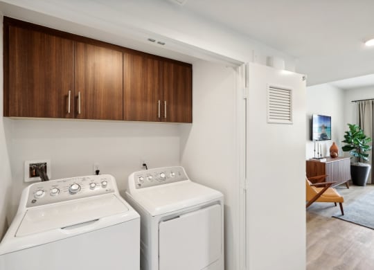 a washer and dryer in a laundry room with a living room and kitchen at The Max on Jefferson Apartments, California, 92562