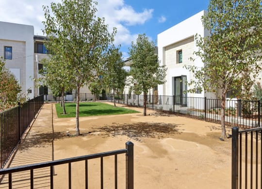 a courtyard with trees and a fence and apartments in the background at The Max on Jefferson Apartments, Murrieta