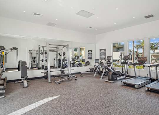 A spacious gym with a variety of equipment including treadmills, weights, and exercise machines at The Max on Jefferson Apartments, California, 92562