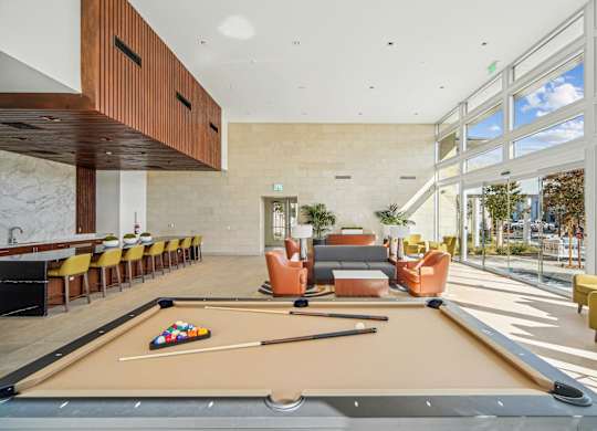 A pool table is in the middle of a room with a lot of chairs. at The Max on Jefferson Apartments, Murrieta, California