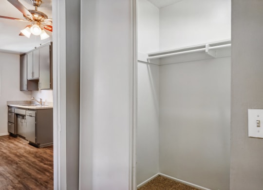 an empty room with an open door to a kitchen and a ceiling fan