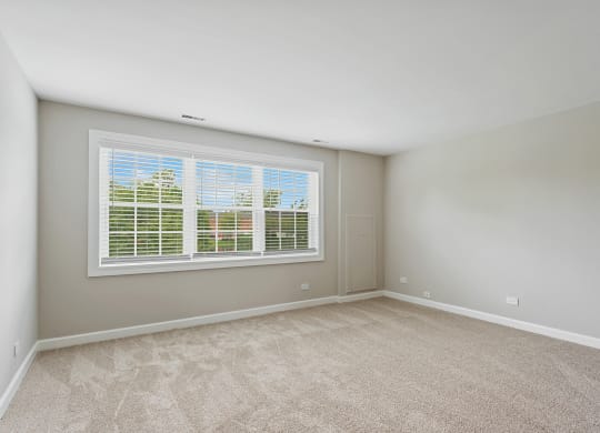 a bedroom with a large window and beige carpet at The Hinsdale, Illinois