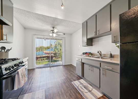 A kitchen with a black refrigerator and wooden floors.