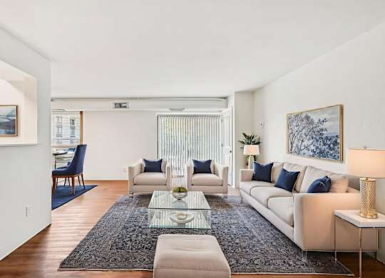 A living room with a white couch, a glass coffee table, and a rug.