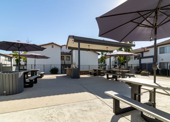 a patio with picnic tables and umbrellas in front of buildings at Alturas Paso Robles Apartment Homes, Paso Robles