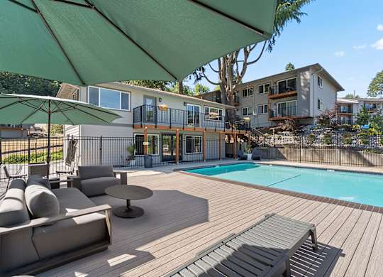 A wooden deck with a green umbrella over a pool.
