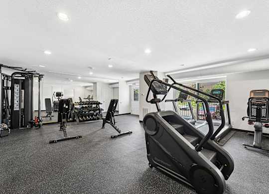 A black treadmill is in the foreground of a well-equipped gym.