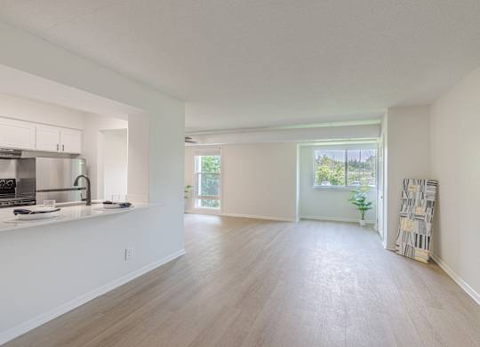 A spacious, empty room with a kitchen area to the left and a doorway leading to another room.