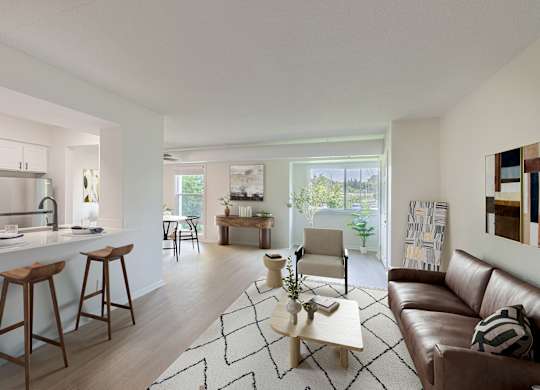 A modern living room with a brown leather couch and a white kitchen area.