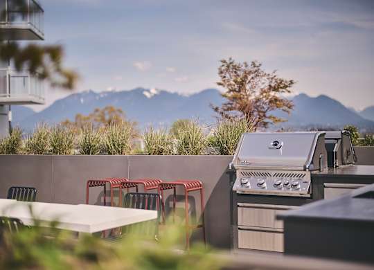 A barbecue grill is on a patio with a table and chairs.