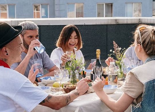 a group of people sitting around a table eating and drinking wine