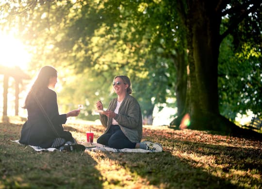 two women sitting in the park talking and drinking wine
