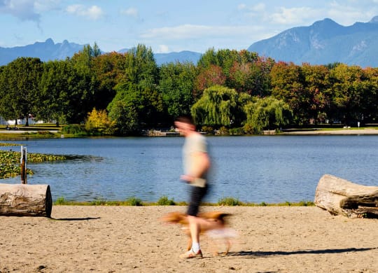 a man running with his dog on the beach near a lake