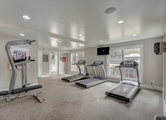 a gym with treadmills and other exercise equipment in a room with windows and white walls