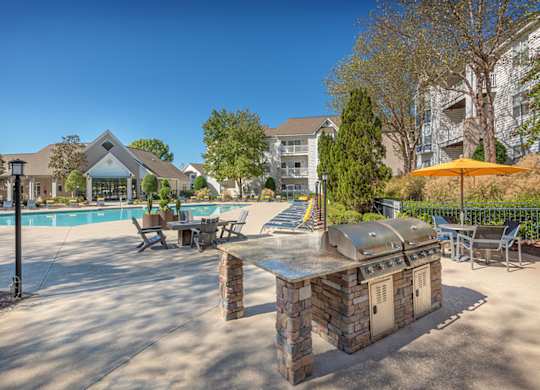 A poolside area with a stone BBQ and chairs.
