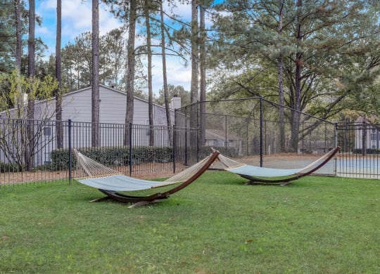 two hammocks in the grass in front of a fence