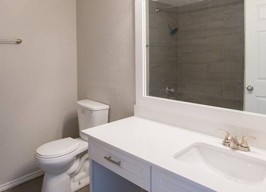 A white bathroom with a toilet, sink and mirror.