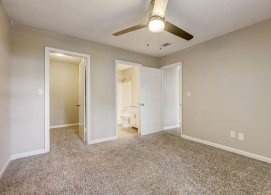 a bedroom with light colored walls and carpet and modern ceiling fan looking into a bathroom at Veridian Sandy Springs