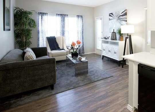 A living room with a grey couch, a white chair, and a glass coffee table.
