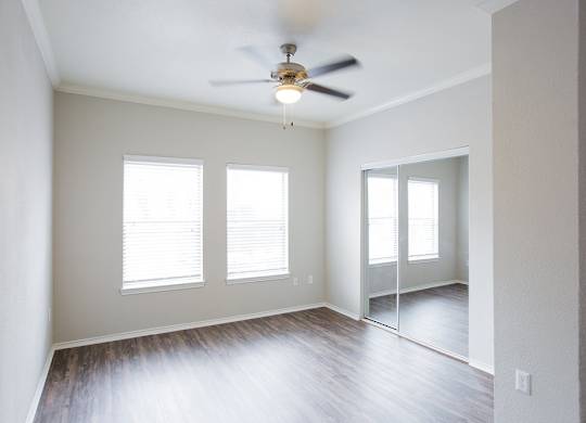A room with a ceiling fan and three windows.
