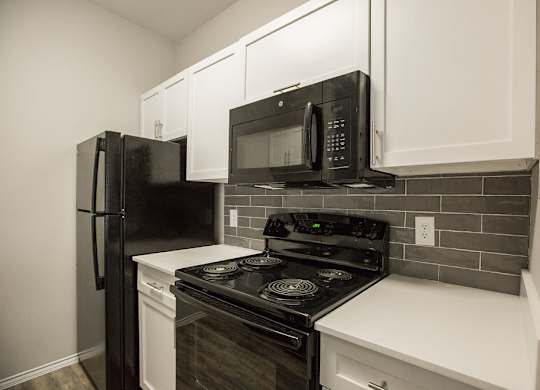 A black refrigerator and microwave in a kitchen with white cabinets.