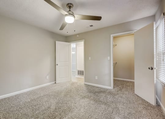 an empty living room with a ceiling fan and a door to a bathroom
