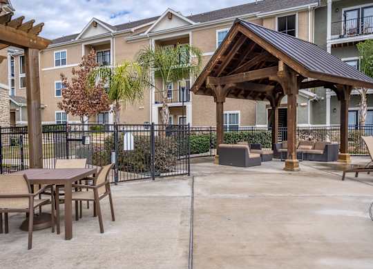 A patio with a table and chairs is surrounded by a black fence and a building in the background.