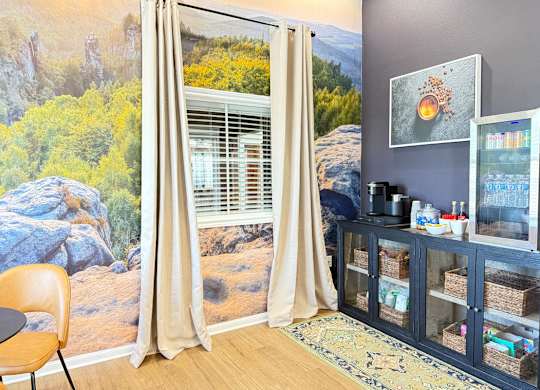 A room with a large mural of a landscape behind a window with beige curtains.