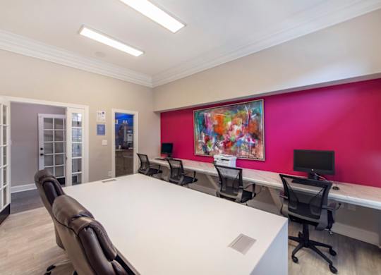 A conference room with a white table and chairs, a pink wall, and a painting on the wall.