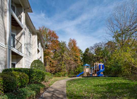 A playground with a blue slide is located in front of a white building.