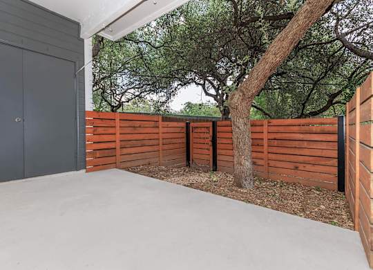 A concrete patio with a grey door and a brown fence.