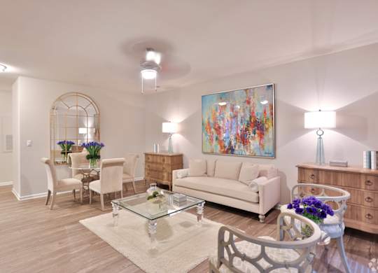 A living room with a white couch, a glass coffee table, and a painting on the wall.