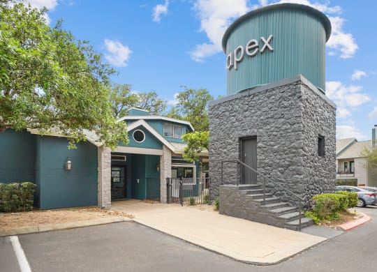 the entrance of apex apartments with a water tower and sign that says apex