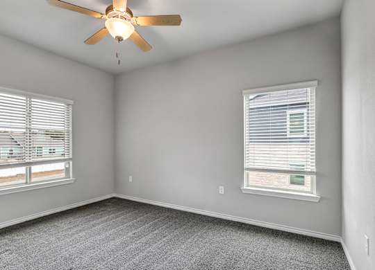 an empty bedroom with a ceiling fan and two windows