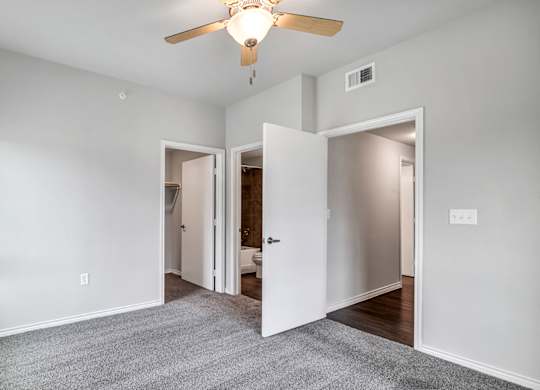 a bedroom with a ceiling fan and a door to a bathroom