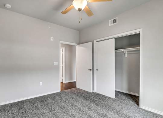 an empty bedroom with a ceiling fan and closet