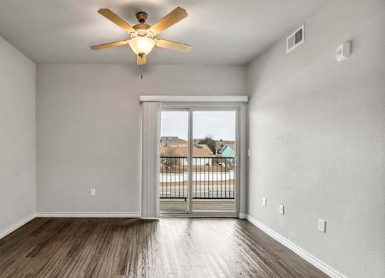 an empty living room with a ceiling fan and a door to a balcony
