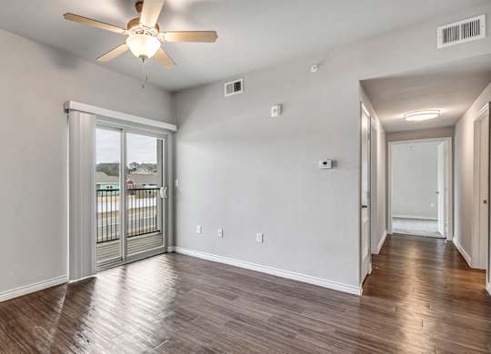 an empty living room with a ceiling fan and a balcony
