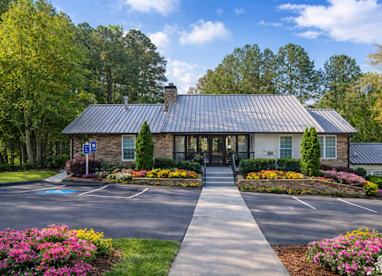 The leasing office with a white roof and a glass door is surrounded by trees and bushes.